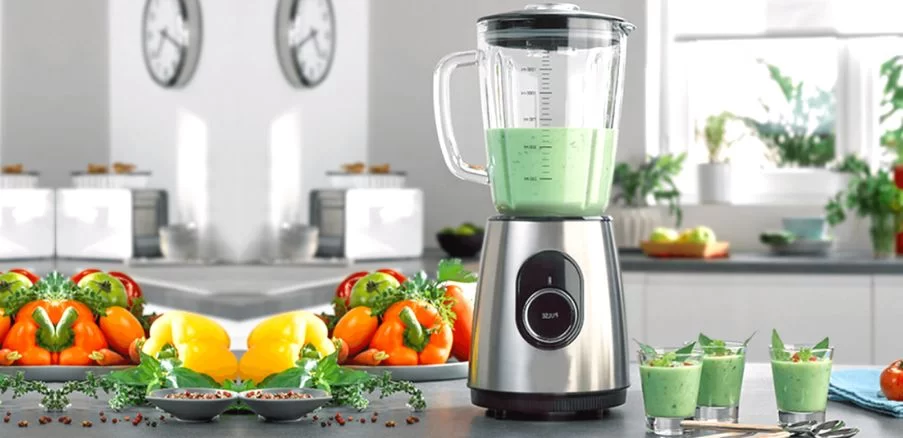 mixer vertical cu continut verde, asezat pe masa, langa legume si pahare cu suc verde